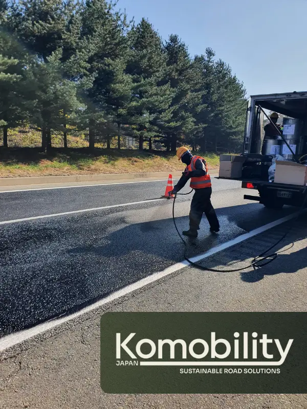 アスファルト舗装に冷間材料を散布する作業員と施工車両